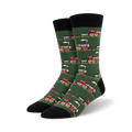 Pair of crew socks with a repeating pattern of red and gray vintage train designs on a green background. Black cuff.