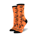 A pair of women's crew socks in bright orange. The socks are covered in a pattern of black owls sitting in bare trees against a background of small white stars and crescent moons.