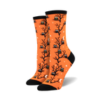 A pair of women's crew socks in bright orange. The socks are covered in a pattern of black owls sitting in bare trees against a background of small white stars and crescent moons.