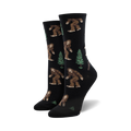 Pair of women's crew socks. Black background with repeating pattern of brown Bigfoot figures and green evergreen trees.