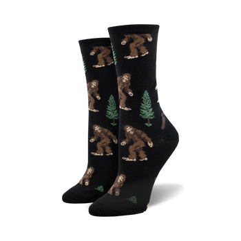 crew length socks for women with pattern of bigfoot creatures walking amidst green pine trees  