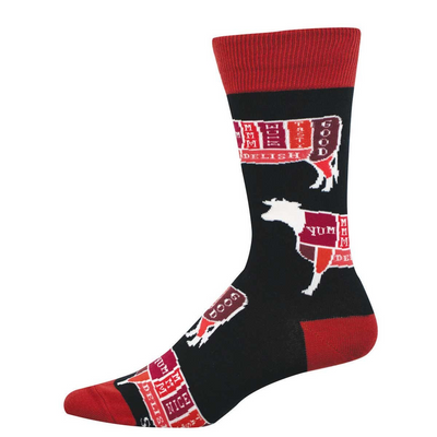 Black crew socks with red cuffs, heel, and toe. Features white outlines of cattle divided into colorful butcher cuts labeled 'YUM' and 'DELISH.'