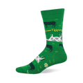 Green crew sock with a "Cow Tipping" design. Features dark silhouette cows, white and grey spotted upside-down cows, yellow text, and white flowers.