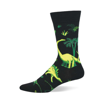 Black crew sock with vibrant yellow-green dinosaurs and green prehistoric trees/foliage. Long-necked and spiky dinosaurs visible.
