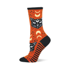 Orange crew sock with black mystic cats, white eyes, crescent moons, and stars. Features black toe, heel, cuff, and striped side panel.