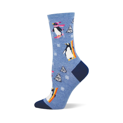 Light blue crew sock with skiing and snowboarding penguins, white snowflakes, and snow-covered pine trees. Dark blue heel and toe.