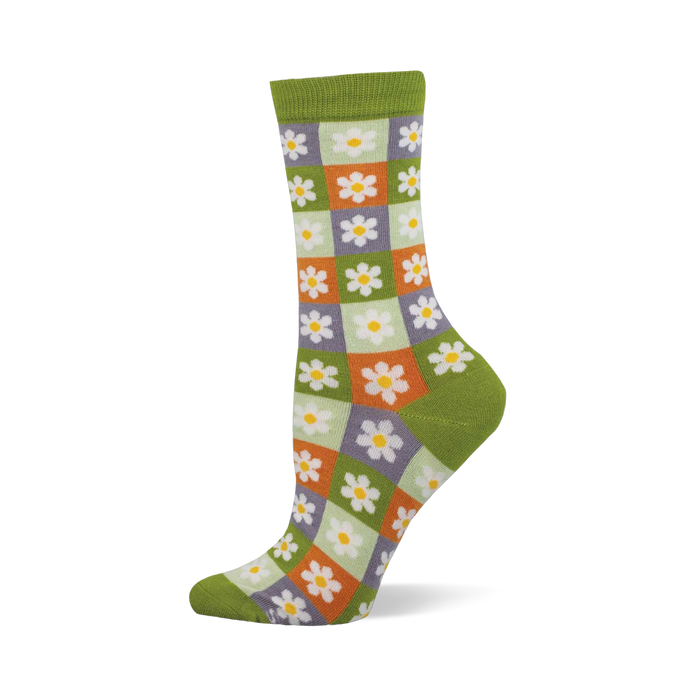 Side view of a crew sock with a checkerboard of light green, orange, and purple squares, each with a white daisy. Dark green cuff, heel, and toe.