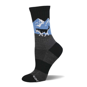 A crew sock featuring a black and white husky running across a light blue background with white mountains. Grey textured mid-foot and black cuff/toe.