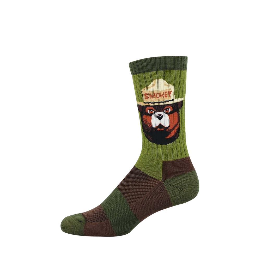 A green crew sock featuring Smokey Bear's head in a tan ranger hat with "SMOKEY" text. The sock has green and brown textured patterns.