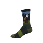 Crew sock with a bald eagle perched on a stump, dark pine trees, and blue sky. Green and dark green stripes on foot.