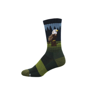 Crew sock with a bald eagle perched on a stump, dark pine trees, and blue sky. Green and dark green stripes on foot.