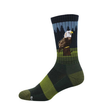 Crew sock with a bald eagle perched on a stump, dark pine trees, and blue sky. Green and dark green stripes on foot.