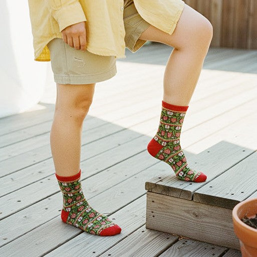 Legs in khaki shorts wearing red-trimmed green strawberry knit crew socks stepping up on a wood deck. [lf]