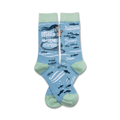 light blue socks with a green cuff. pattern of dark blue fish and mermaid with black hair and green tail. text reads 'kinda pissed about not being a mermaid.'   