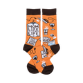 A pair of orange crew socks with a brown cuff. The socks show illustrations of coffee, wine, laundry, and a shopping list that says 'Mom Life is the Best Life'.