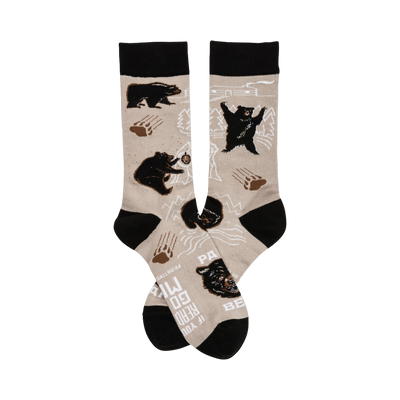 A pair of beige crew socks with a playful design featuring black bears, paw prints, and mountain outlines. The cuffs are black.