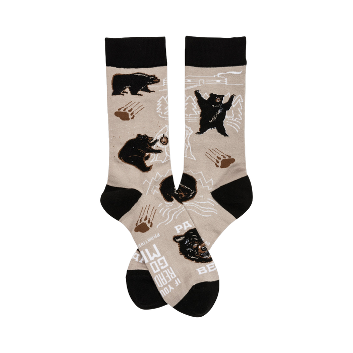 A pair of beige crew socks with a playful design featuring black bears, paw prints, and mountain outlines. The cuffs are black. }}