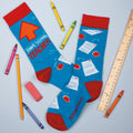Lifestyle flat lay photo of 'Awesome Teacher' socks on a light blue background with crayons, a ruler, and an eraser. [lf]