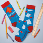 Lifestyle flat lay photo of 'Awesome Teacher' socks on a light blue background with crayons, a ruler, and an eraser. [lf]