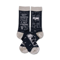 Pair of navy blue crew socks with a light beige cuff. One sock shows a building with a cat in the window, the other says, 'You're not drinking alone if your cat is home'.