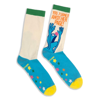 Flat lay of crew socks with a cream shaft, green cuff, blue foot, yellow toe, colorful stars, and panicked Grover graphic.