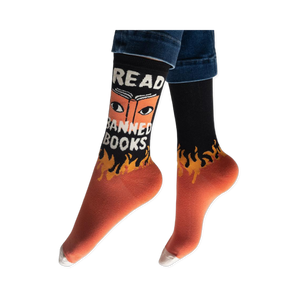 Person wearing the black and orange Read Banned Books socks, showing the white text and eye graphic facing forward.