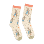 Pair of Peter Rabbit crew socks in light beige, with peach ruffled cuffs and olive green toes, standing upright.