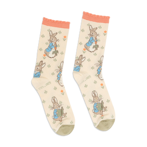 Pair of Peter Rabbit crew socks in light beige, with peach ruffled cuffs and olive green toes, standing upright.