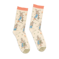 Pair of Peter Rabbit crew socks in light beige, with peach ruffled cuffs and olive green toes, standing upright.