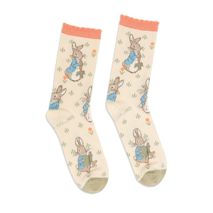 Pair of Peter Rabbit crew socks in light beige, with peach ruffled cuffs and olive green toes, standing upright.