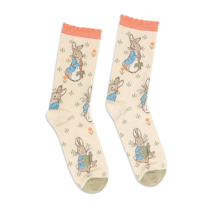 Pair of Peter Rabbit crew socks in light beige, with peach ruffled cuffs and olive green toes, standing upright.