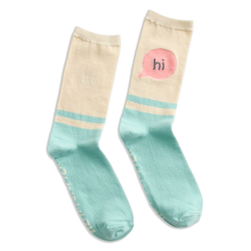 A pair of crew socks with a cream upper half, light blue lower half, and a pink speech bubble graphic on one sock containing the word 'hi'.