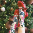 Sheer floral socks worn with glossy red Mary Jane shoes featuring rose details, posed by a lit Christmas tree.