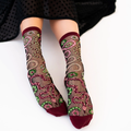 Person sitting wearing sheer snake pattern socks with burgundy trim, a black polka dot skirt draped over their knees.