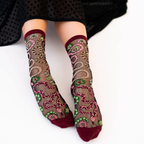 Person sitting wearing sheer snake pattern socks with burgundy trim, a black polka dot skirt draped over their knees.