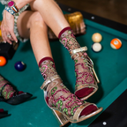 Legs resting on a green pool table wearing sheer snake pattern socks and metallic gold strappy heels next to billiard balls.