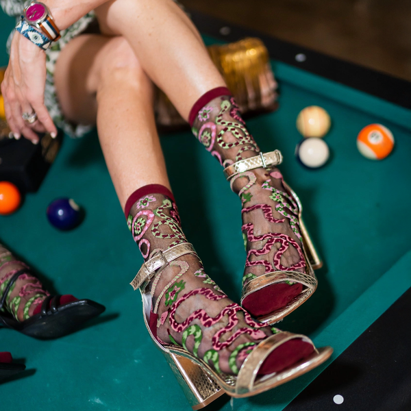[lf] Legs resting on a green pool table wearing sheer snake pattern socks and metallic gold strappy heels next to billiard balls.