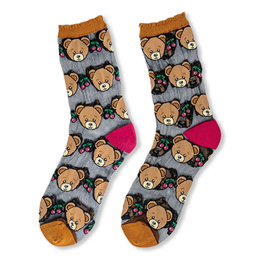 Flat lay of sheer mesh socks with opaque teddy bear faces, red cherries, mustard ruffled cuffs, and bright pink heels.