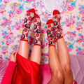 Flat lay of sheer mesh socks with opaque teddy bear faces, red cherries, mustard ruffled cuffs, and bright pink heels.