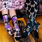 Two pairs of legs by a gold table. Left wears sheer cat socks, right wears opaque black socks with butterflies.