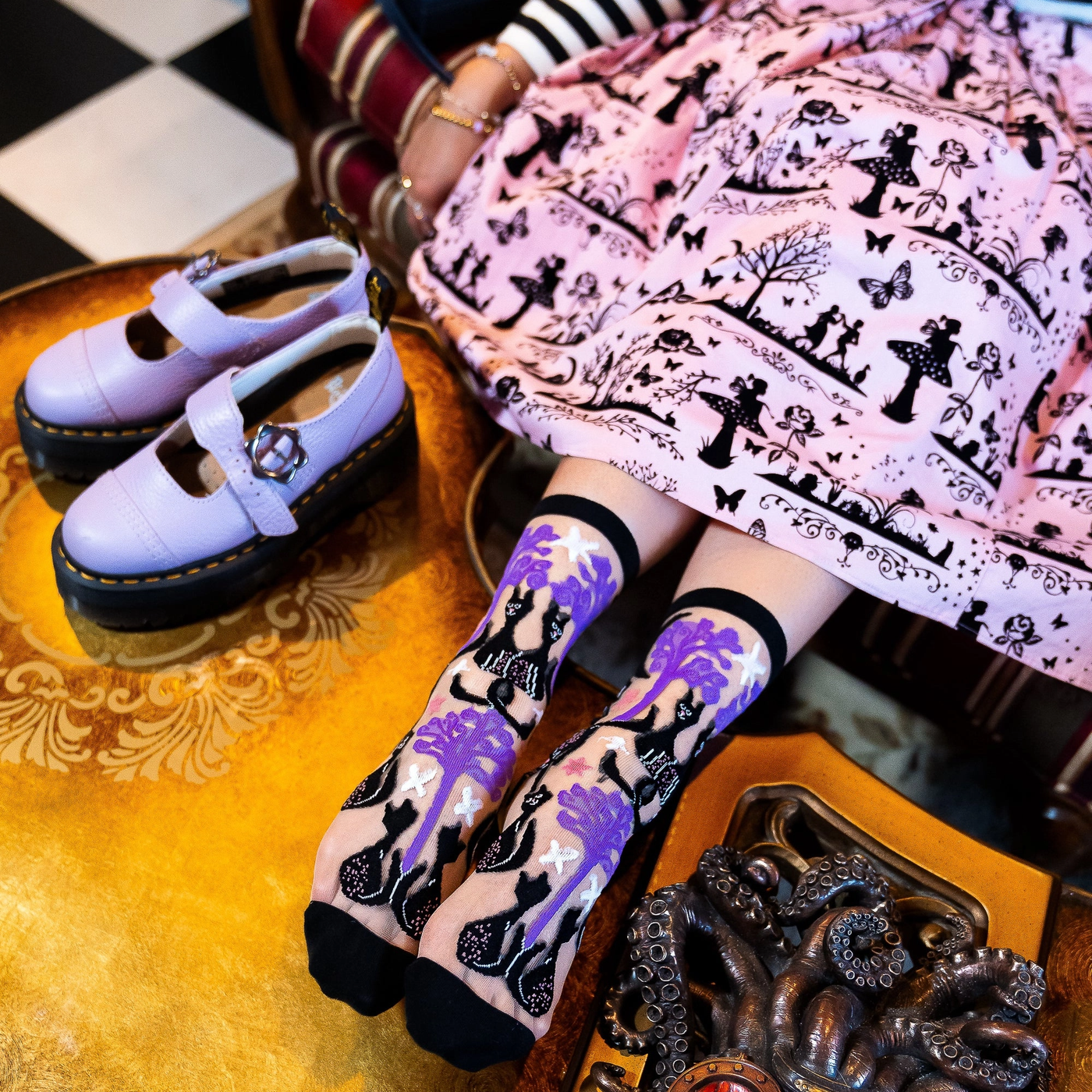Pair of sheer crew socks featuring a pattern of black cats, twisted purple trees, moons, and stars with solid black cuffs.