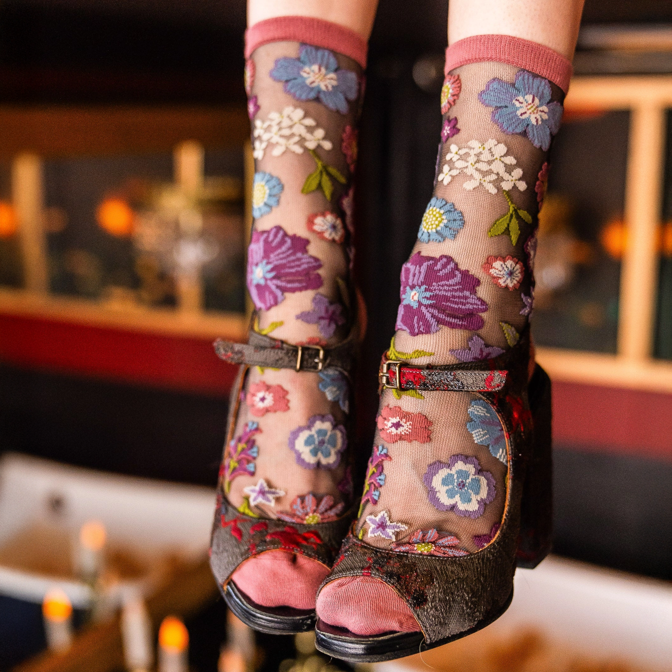 Close up of feet dangling in sheer mesh floral socks worn with chunky dark platform heels against a blurred background