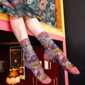 Person legs dangling over a colorful painted ledge showing sheer floral socks and a dark red wall in the background