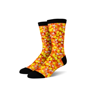 A pair of crew socks covered in a candy corn print. The socks are predominantly orange, yellow, and white, with a black cuff.