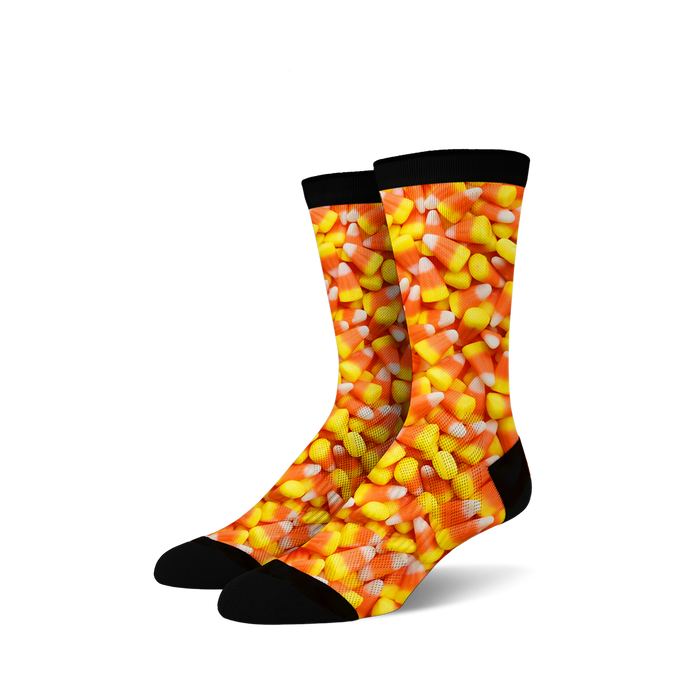 A pair of crew socks covered in a candy corn print. The socks are predominantly orange, yellow, and white, with a black cuff.