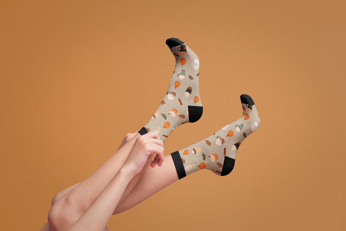 Lifestyle shot of a model pulling up their Pumpkin Spice Latte socks against a burnt orange background. [lf]