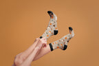 Lifestyle shot of a model pulling up their Pumpkin Spice Latte socks against a burnt orange background. [lf]