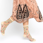 Person walking wearing sheer floral rosette socks paired with a detailed peach beaded and sequined vintage dress.