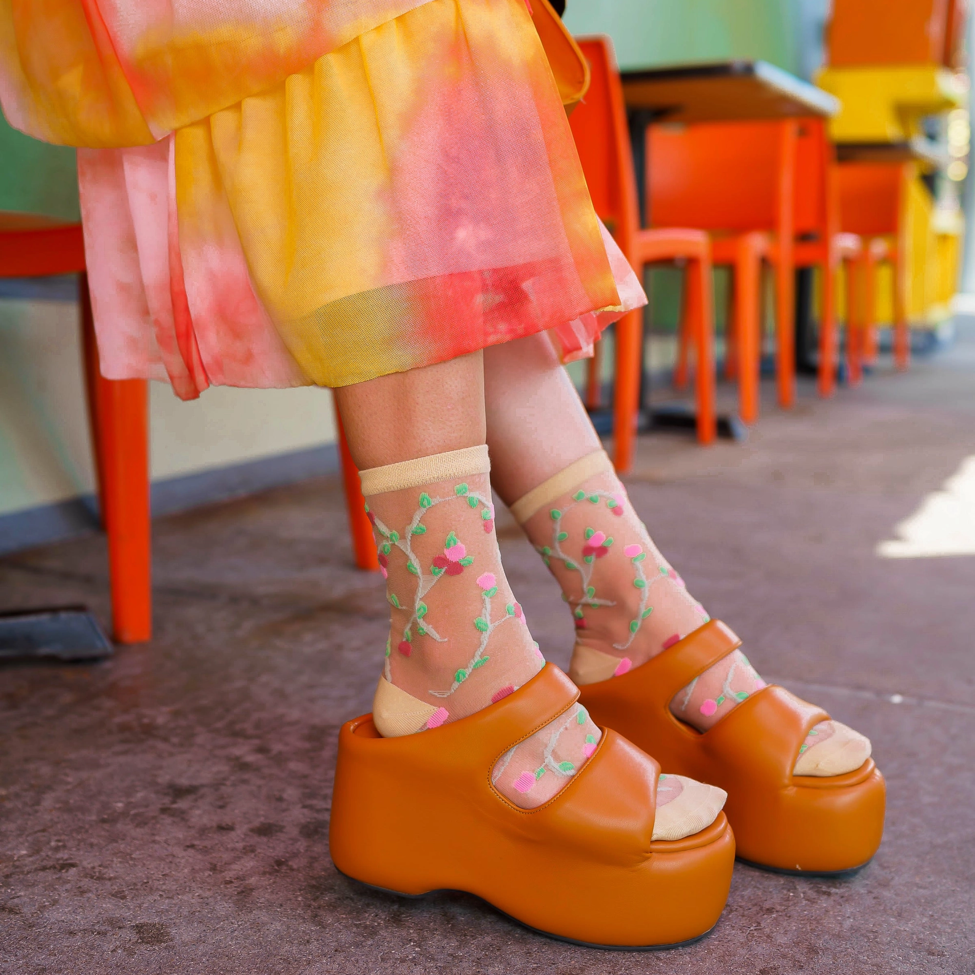 Close up of sheer rosette socks worn with chunky orange platform sandals and a bright orange and pink tie-dye skirt.