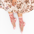 Person sitting on a white surface wearing a floral skirt and sheer pink cherry blossom socks.